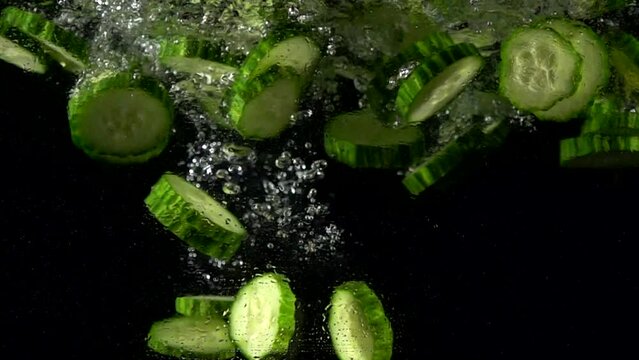 Super slow motion of falling fresh cucumber slices in water. Isolated on black background. Filmed on high speed cinema camera, 4k 1000fps.
