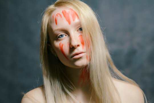Portrait of young woman with paint on her face on dark background.