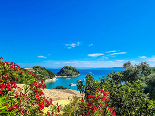 Red Flowers Frame Magnificent Blue Lagoon: Turquoise Waters, Azure Sea, and Beach Bliss in a Greek Island Paradise