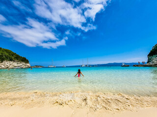Fototapeta na wymiar A Girl Enters Azure Waters. Turquoise Beach Sea View, blue sky and white clouds