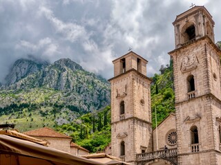 Under the limestone mountains and dramatic clouds in Old Kotor, Montenegro, a low angle view of the two stone bell towers of the landmark 12th century Cathedral of Saint Tryphon.