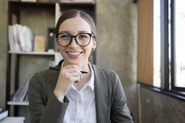 Portrait of smiling pretty young business woman in wearing glasses sitting on her workplace office, business finance concept.