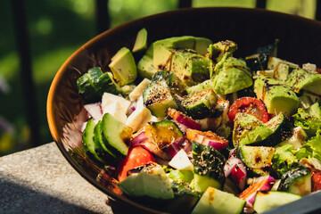 Avocado mix of vegetables salad in daytime outdoors. Fresh salad with tomatoes, avocado, lettuce onion cucumber. Healthy and detox food concept. Ketogenic diet