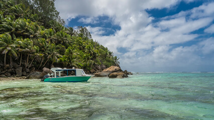 The boat is moored off the coast of a tropical island overgrown with palm trees. Boulders in...