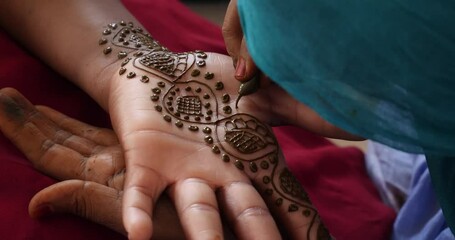 A close up shot of a black woman hand being painted with henna.