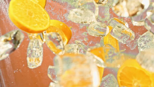 Citrus orange slices and ice fall or explode in super slow motion 1000fps on orange background.Juicy sweet orange and fly ice cube or water splash or pours drops juice in super slow motion on 1000fps