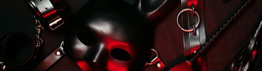 Set of erotic toys from a sex shop on a dark red background. Mask, leather belt, choker, handcuffs,...