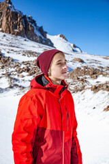 Fototapeta na wymiar Young happy man in red hat enjoys sunny day in snow mountains.