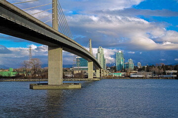 Fototapeta premium Sky-train bridge linking Richmond and Vancouver City over the Fraser River, city on the opposite bank, stormy sky with clouds on a background 