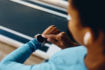 Close up of African American athlete adjusts her fitness tracker while working out in gym.