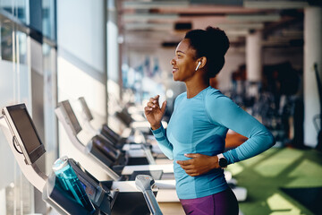 Happy black athletic woman runs on treadmill while working out in gym.