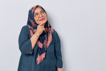 Beautiful pensive elderly Asian muslim woman 50s wearing hijab in glasses looking aside at empty space, touching chin, thinking about something on white background. People islam religious concept