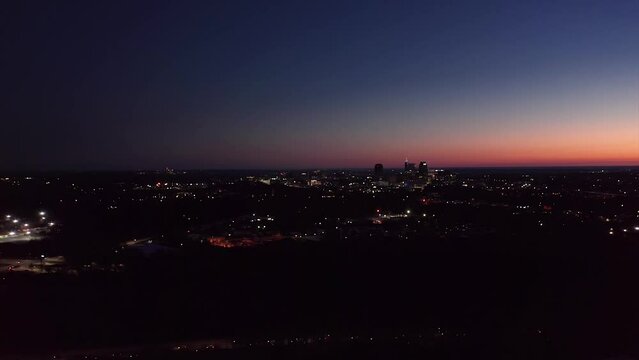 Aerial shot of cars driving on highway at night. Raleigh NC skyline in distance.