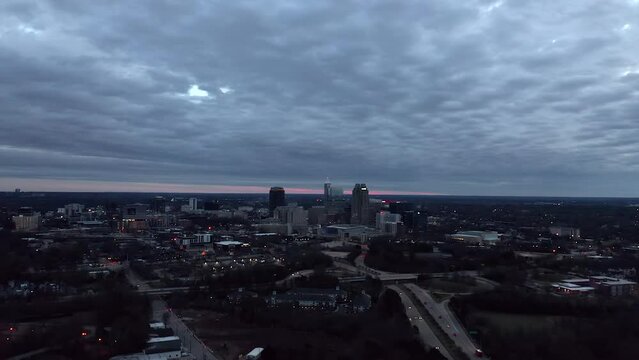 Aerial orbit around Raleigh, North Carolina during cloudy sunset. Urban American city at night and dusk.