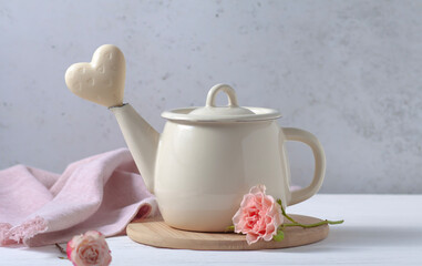 A teapot on the table, a pink rose and a white chocolate heart. Valentine's Day postcard