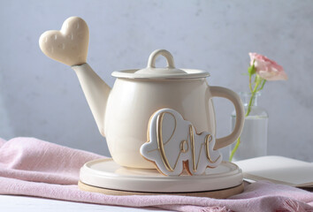 A teapot on the table, a pink rose and a white chocolate heart. Valentine's Day postcard