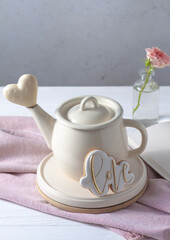 Obraz na płótnie Canvas A teapot on the table, a pink rose and a white chocolate heart. Valentine's Day postcard