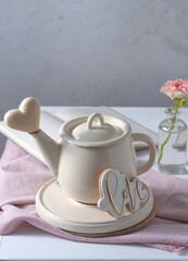 A teapot on the table, a pink rose and a white chocolate heart. Valentine's Day postcard