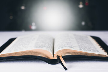 An open Bible on the table. Prayer. Scripture. On the background of the Christmas tree. Light and garlands