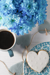 A cup, a bouquet of blue flowers and gingerbread in the shape of a heart