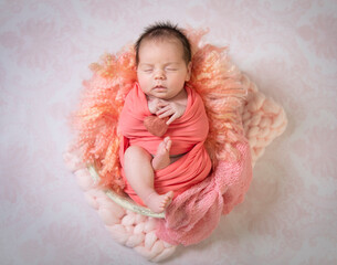 Sleeping newborn infant girl in soft pastel color wrap holding tiny heart - 569438599