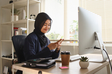 Muslim woman using smartphone in office. Entrepreneur businessman, freelancer, sits at her office desk.