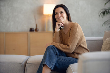 Fototapeta premium Happy dreamy middle aged woman sitting on sofa at home and looking at camera
