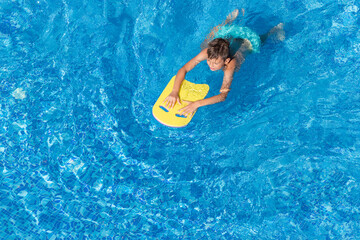 Boy child swim in swimming pool using a board. Active wellness summer vacation in resort hotel....