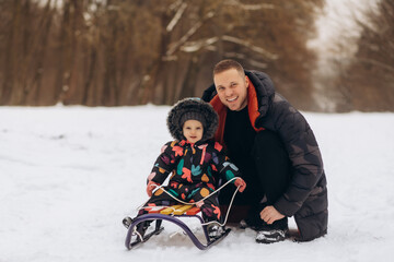 Father and daughter sitting on sled in snow field, smiling, portrait