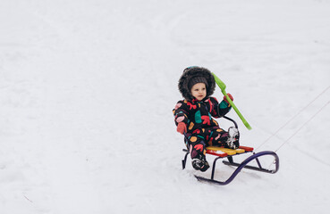 Fototapeta na wymiar Little girl sledging downhill an having fun. Pink sledge and jacket, colorful scarf.