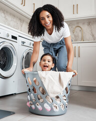Happy mother with her child in a washing basket at their home while doing laundry together....