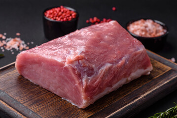 A piece of raw fresh pork on a wooden cutting board with spices and herbs