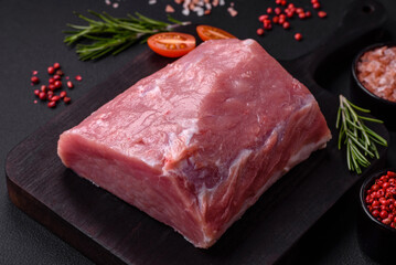 A piece of raw fresh pork on a wooden cutting board with spices and herbs