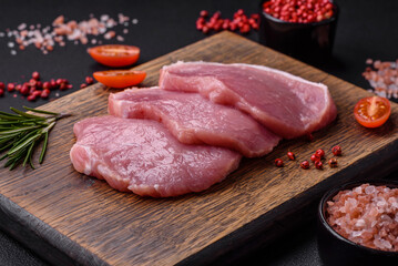 A piece of raw fresh pork on a wooden cutting board with spices and herbs