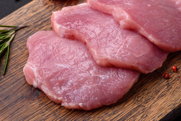 A piece of raw fresh pork on a wooden cutting board with spices and herbs