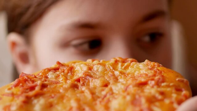 Close-up, a child bites off a piece of delicious pizza looks away, selective focus.