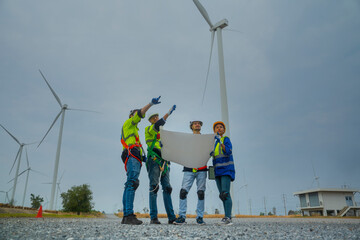 Group of Asian male and female engineer friends holding a blueprint looking at the construction of a turbine power station in a turbine field