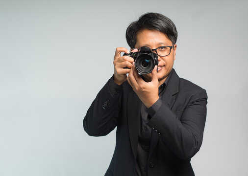 Photographer in a suit holding the digital camera while standing on a gray background