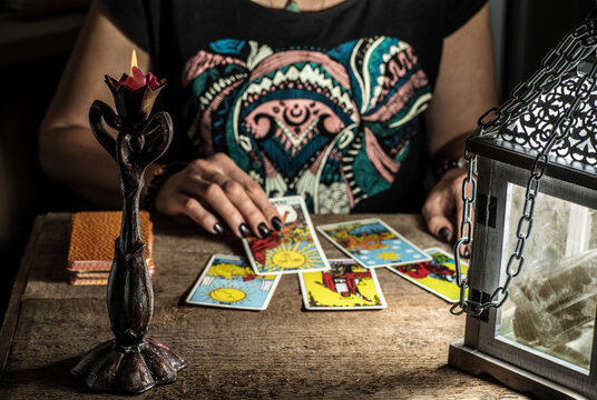 The fortune teller lays out on a wooden table the tarot cards by the light of a lantern and a candle. Selective focus.