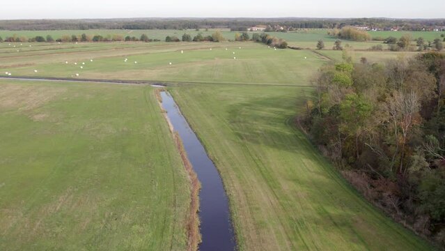 Areal drone footage of water channel and vast farming fields with autumn colors taken at place called Uetz in Brandenburg, Germany. Peaceful and tranquil atmosphere.