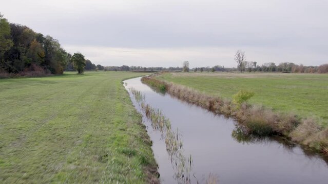 Ascending areal drone footage of water channel and vast farming fields with autumn colors taken at place called Uetz in Brandenburg, Germany.