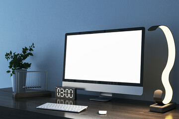 Close up of creative designer desktop with empty white mock up computer monitor, supplies and various items on blue concrete wall background. 3D Rendering.