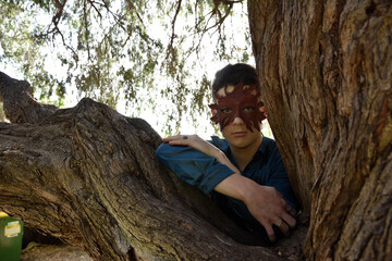 portrait of handsome brunette man wearing fantasy medieval prince costume with greenmail leather mask and romantic silk shirt, posing in a forest location with tree foliage background. 