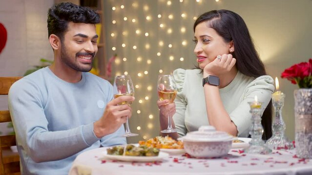 Happy romantic couple having drinks or wine by talking each other at candle light dinner at home - concept of romantic evening, dating and love or affection.