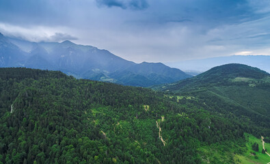 Aerial view of a beautiful landscape from Bucegi mountains in Romania, with forest green trees and cloudy sky. Travel to Romania.