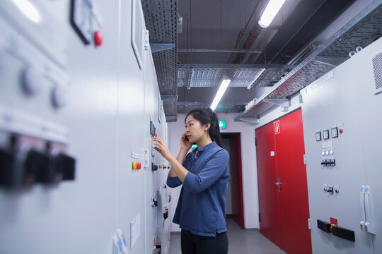 Young female engineer updating control panel using mobile phone in an industrial plant, Freiburg im Breisgau, Baden-Württemberg, Germany