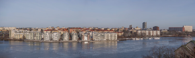Fototapeta na wymiar Panorama, view from the hill Ormberget over the districts Essingen islands and Kungsholmen, waterfront apartments at a bay of the Mälaren se, a sunny snowy winter day in Stockholm