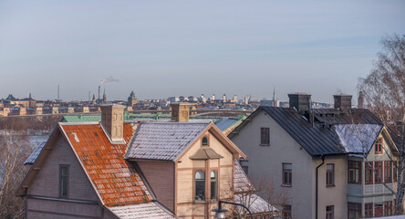 Old wood apartment houses with chimneys and dorms, background skyline of down town, a sunny snowy winter day in Stockholm