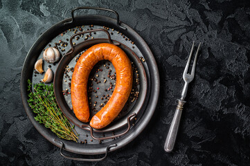 Smoked sausage with thyme and spices in a steel tray. Black background. Top view