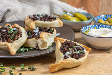 Traditional cookie Hamantasch with beef meat, tahini sauce and fresh thyme for Jewish holiday Purim on wooden background.